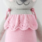 Close-up of Claire the Koala - Little 13" by Cuddle + Kind, a knitted stuffed animal in a pink dress with scalloped edging and tie straps, showing her upper body and part of her face, ready for a magical adventure.