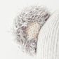 Close-up of a knitted grey and cream ear on Claire the Koala - Regular 20" by Cuddle + Kind, attached to a textured fabric—ideal for snuggling with friends during magical adventures or relaxing in your own cozy space.