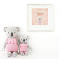 Two Claire the Koala - Little 13" toys by Cuddle + Kind in pink outfits sit beneath a "Daydream believer" picture with playful koala and leaf art, evoking a sweet treehouse or magical treetop scene.