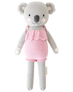 Claire the Koala - Little 13" by Cuddle + Kind is a knitted gray plush toy in a pink ruffled dress, posed upright against a white background—an adorable friend for magical adventures or birthday cuddles on December 3rd.