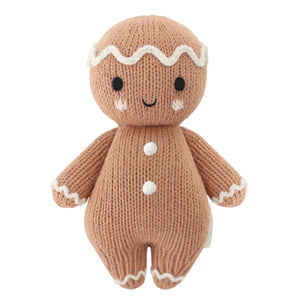 Introducing the Baby Gingerbread - Icing White from Cuddle + Kind—a charming knitted doll featuring a smiling face, white icing details on its head, arms, and legs, and two white buttons on its body. Lovingly handcrafted from soft cotton yarn, this delightful companion is perfect for little ones.