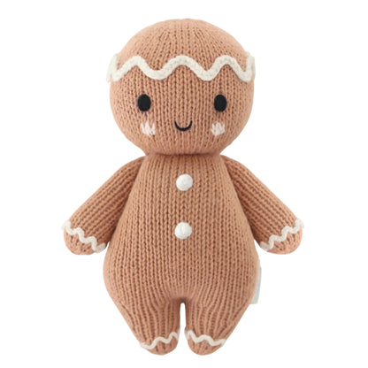 Introducing the Baby Gingerbread - Icing White from Cuddle + Kind—a charming knitted doll featuring a smiling face, white icing details on its head, arms, and legs, and two white buttons on its body. Lovingly handcrafted from soft cotton yarn, this delightful companion is perfect for little ones.