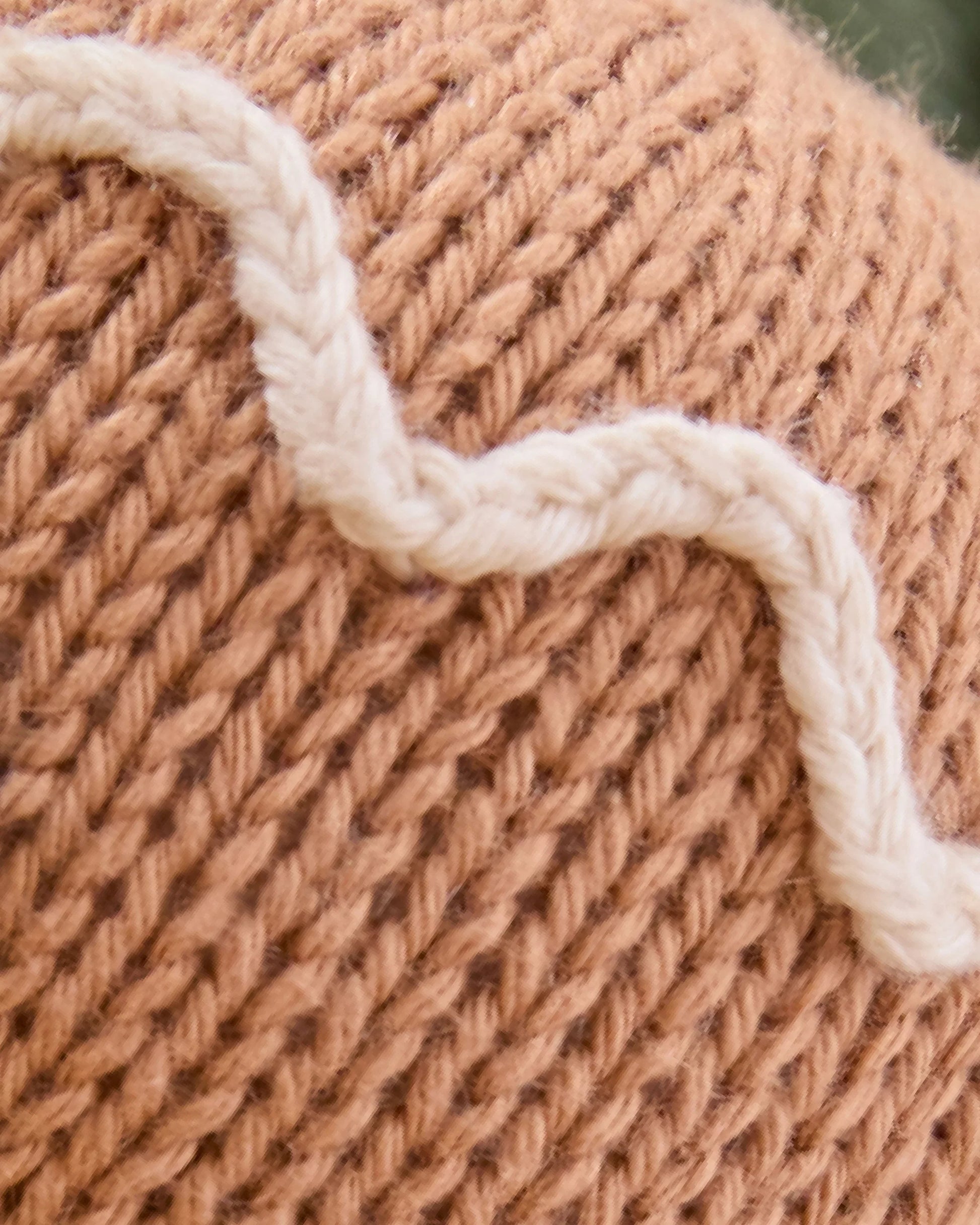 Close-up of the Baby Gingerbread - Icing White by Cuddle + Kind, showcasing brown cotton yarn handcrafted into a knitted fabric with a wavy white yarn pattern stitched on its surface.