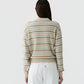 A person stands with their back to the camera, wearing the Guest in Residence Collegiate Stripe Polo in beige and white, paired with white pants against a plain background.