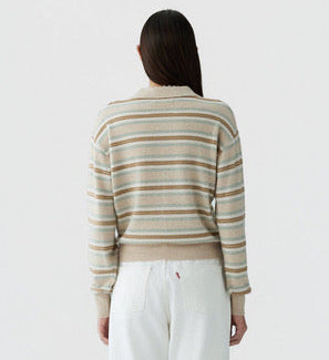 A person stands with their back to the camera, wearing the Guest in Residence Collegiate Stripe Polo in beige and white, paired with white pants against a plain background.