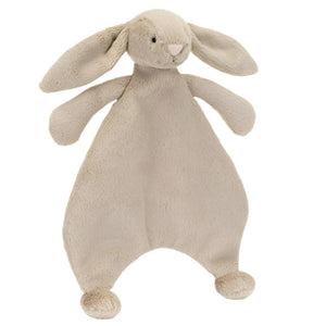 The Jellycat Bashful Beige Bunny Comforter, by Jellycat, features a plush beige design with floppy ears and extended arms, made from recycled fibers. It stands upright on a white background, combining both charm and sustainability.