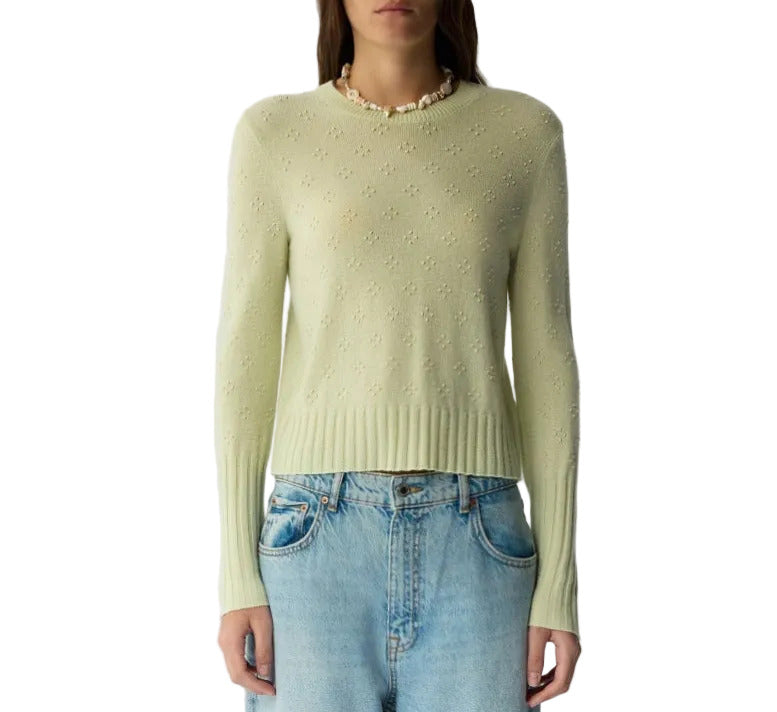 A person wearing the Compass Shrunken Crew sweater by Guest in Residence in light green with a subtle flower pattern and lightweight popcorn stitch, paired with light blue jeans.
