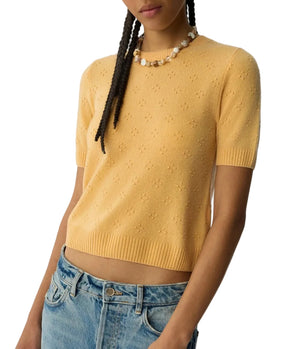 A person wears the Compass Sweater Tee by Guest in Residence in light yellow with a subtle dotted pattern, paired with blue jeans and a pearl necklace. This women's cashmere sweater combines effortless style and comfort.