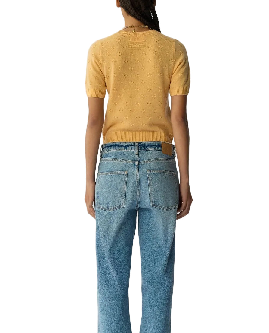 A person stands with their back to the camera, wearing the Compass Sweater Tee by Guest in Residence—a women’s lightweight cashmere short-sleeve sweater in yellow—paired with light blue jeans against a white background.
