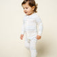 A toddler stands and walks on a light background, dressed in Lou Lou & Company’s Baby Conrad Zipper Footie—silky-soft, white sleepwear featuring small, colorful dotted lines for cozy comfort.