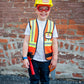 A child beams in front of a brick wall, proudly holding a toy tool while wearing the Great Pretenders Construction Worker Set—complete with helmet, safety goggles, and vest—for fun dress up play.