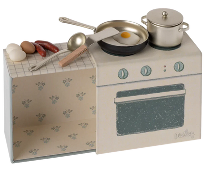 A Maileg Cooking Set designed for mice, featuring a miniature toy stove with a frying pan containing a sunny-side-up egg, a pot, sausages, and three eggs on the countertop. This small kitchen set includes kitchen utensils and an oven, all set against a floral-patterned background—perfect for any kids playset.