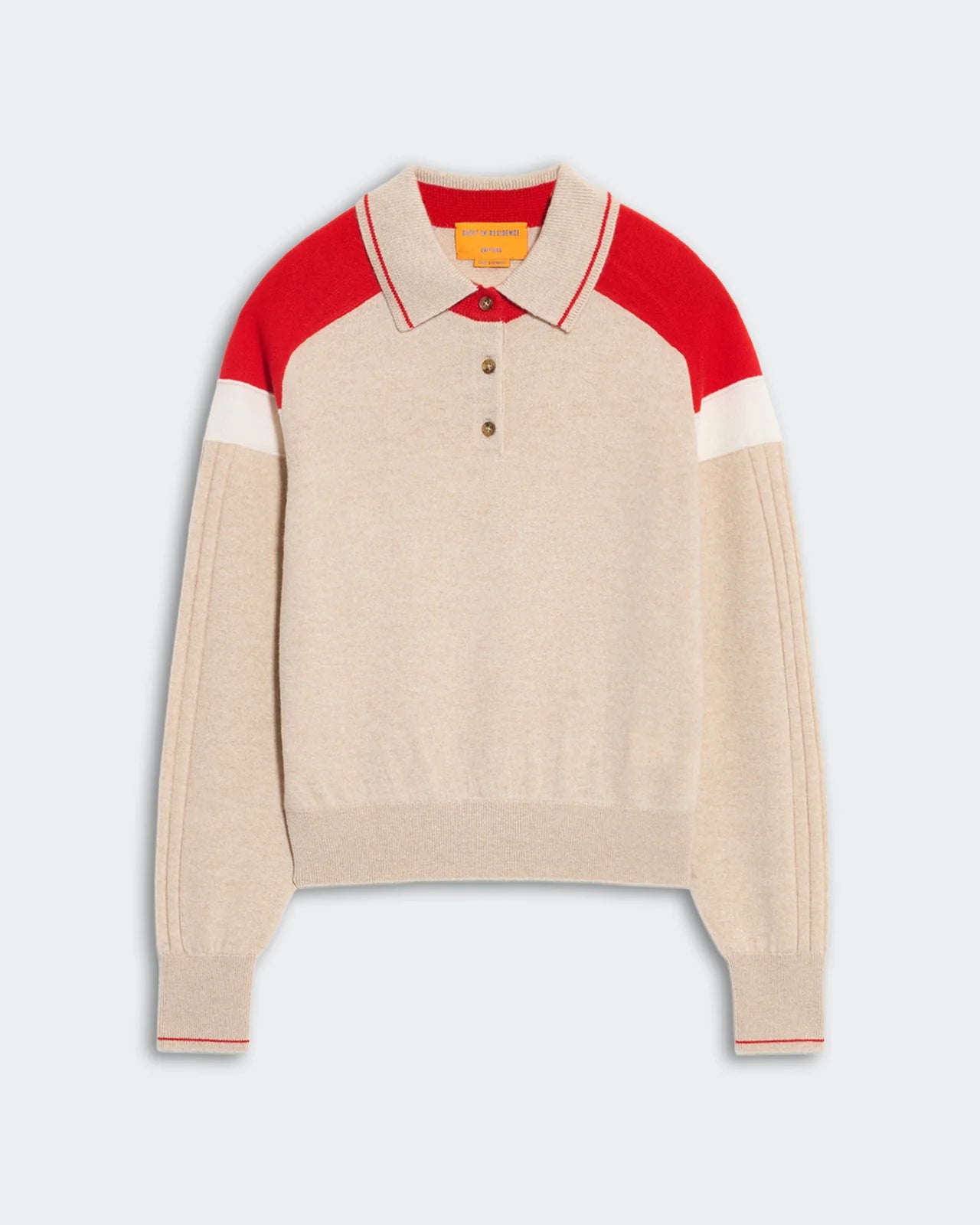 The Alpine Collegiate Polo by Guest in Residence is a beige women’s cashmere sweater featuring red and white color block on the shoulders and collar, long sleeves, and a three-button placket—ideal for elevating your casual style.