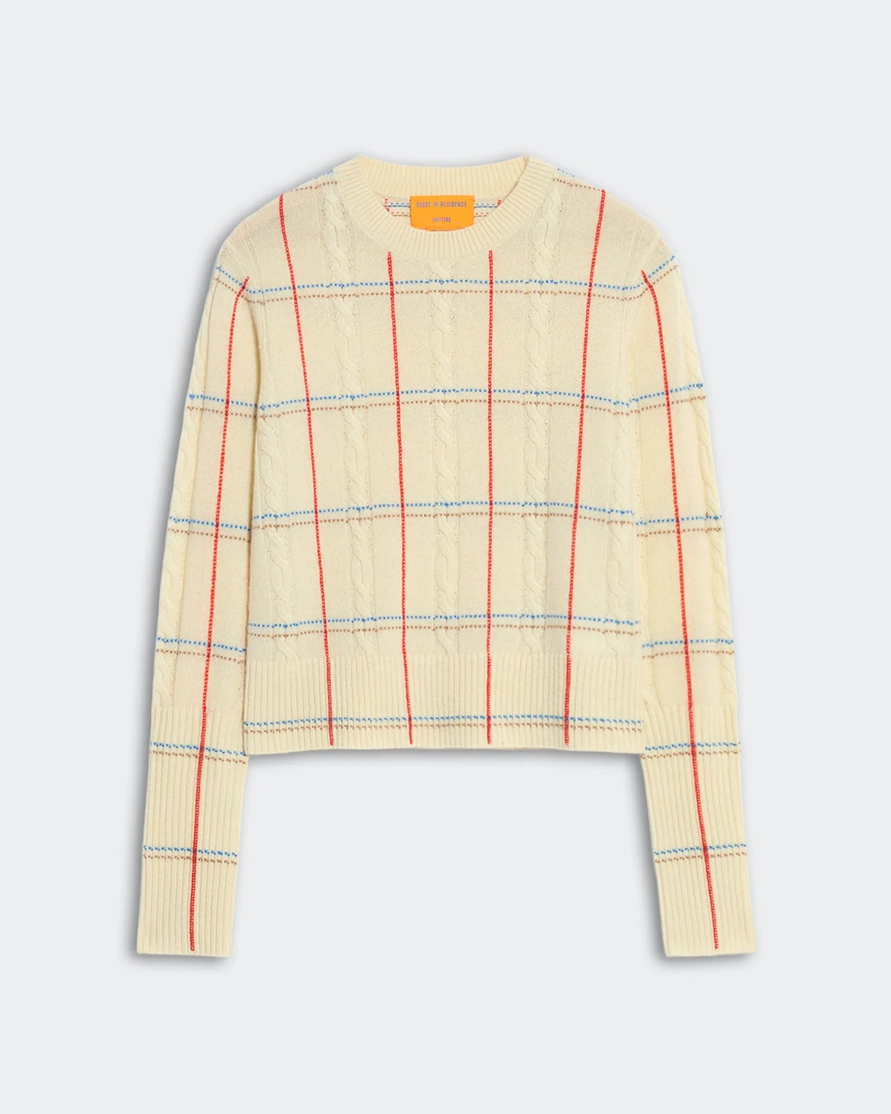 The Shrunken Check Crew by Guest in Residence is a cream cashmere women’s sweater with a red and blue check jacquard pattern, crew neck, and ribbed cuffs and hem.