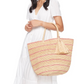 A woman in a white short-sleeve dress holds the Mar Y Sol Costa Tote, a spacious and stylish bag woven with pink stripes and adorned with a decorative tassel.