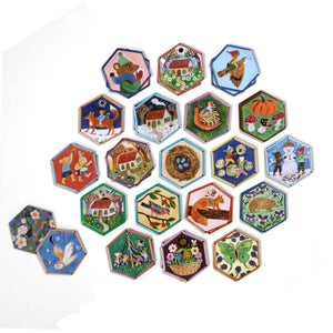 Eeboo’s Cottage Fairies Memory & Matching Game features hexagon-shaped tiles illustrated with charming animals, flowers, cottages, and whimsical fairy scenes—some highlighted with gold foil—arranged in a playful honeycomb pattern on a crisp white background.