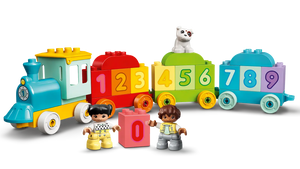 The LEGO® DUPLO® Number Train - Learn To Count by LEGO® features blocks numbered 0-9, two child figures, and a white cat on a green block—an ideal educational toy for toddlers to learn numbers while playing.