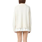 A person stands with their back to the camera, wearing the Guest in Residence Cozy Crew Cashmere Sweater—an oversized white knit with a ribbed neck trim—paired with a short white pleated skirt, set against a plain white background.