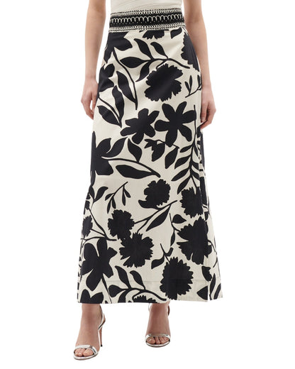 A person is wearing the Figue Cressida Skirt, a black and white floral-patterned, ankle-length skirt with a beaded waistband, paired with open-toe heels.