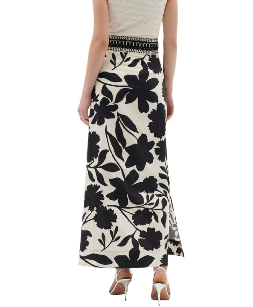 Woman wearing a sleeveless top and the Figue Cressida Skirt, a long, black and white floral cotton poplin skirt with a beaded waistband from Figue, standing with her back to the camera.