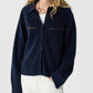 A person with long blonde hair wears the Guest in Residence Cropped Western Shirt in navy with brown stitching, styled over a white top and paired with white pants and a beaded necklace, set against a plain background.