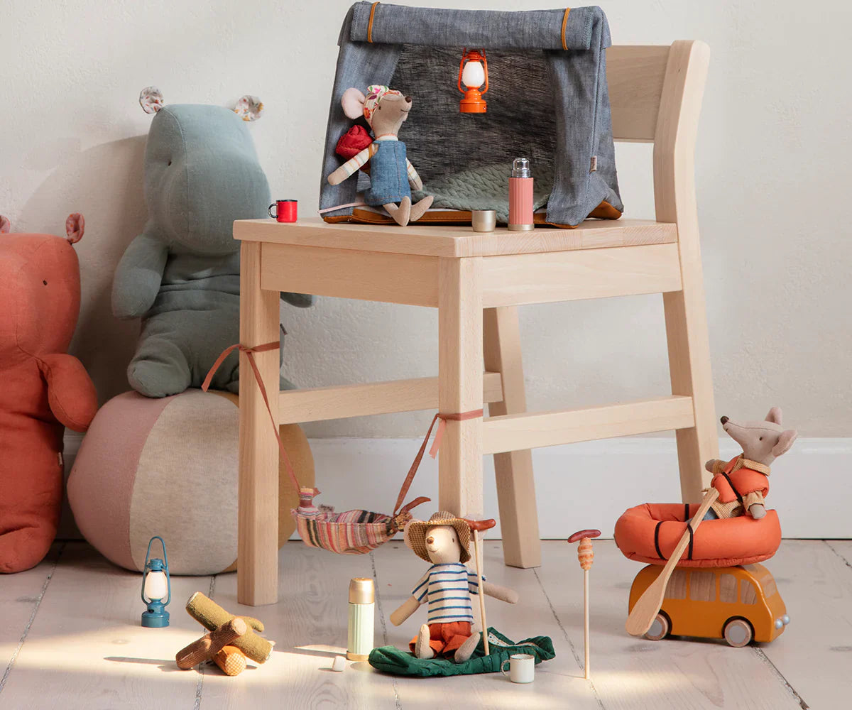 A wooden chair holds a small fabric tent, surrounded by various toy animals and camping accessories, including the Maileg Thermos and Cups - Mint set, a campfire, and toy vehicles on a wooden floor. Hiker mice with magnetic hands add an adventurous touch to the cozy scene.