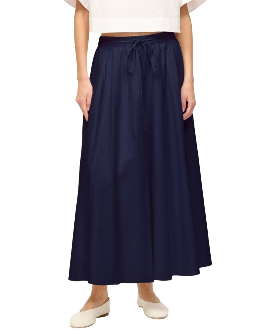 Person wearing a white top, Staud Eden Skirt by Staud with an adjustable drawstring waistband, and white shoes. Only the lower half of the body is visible.