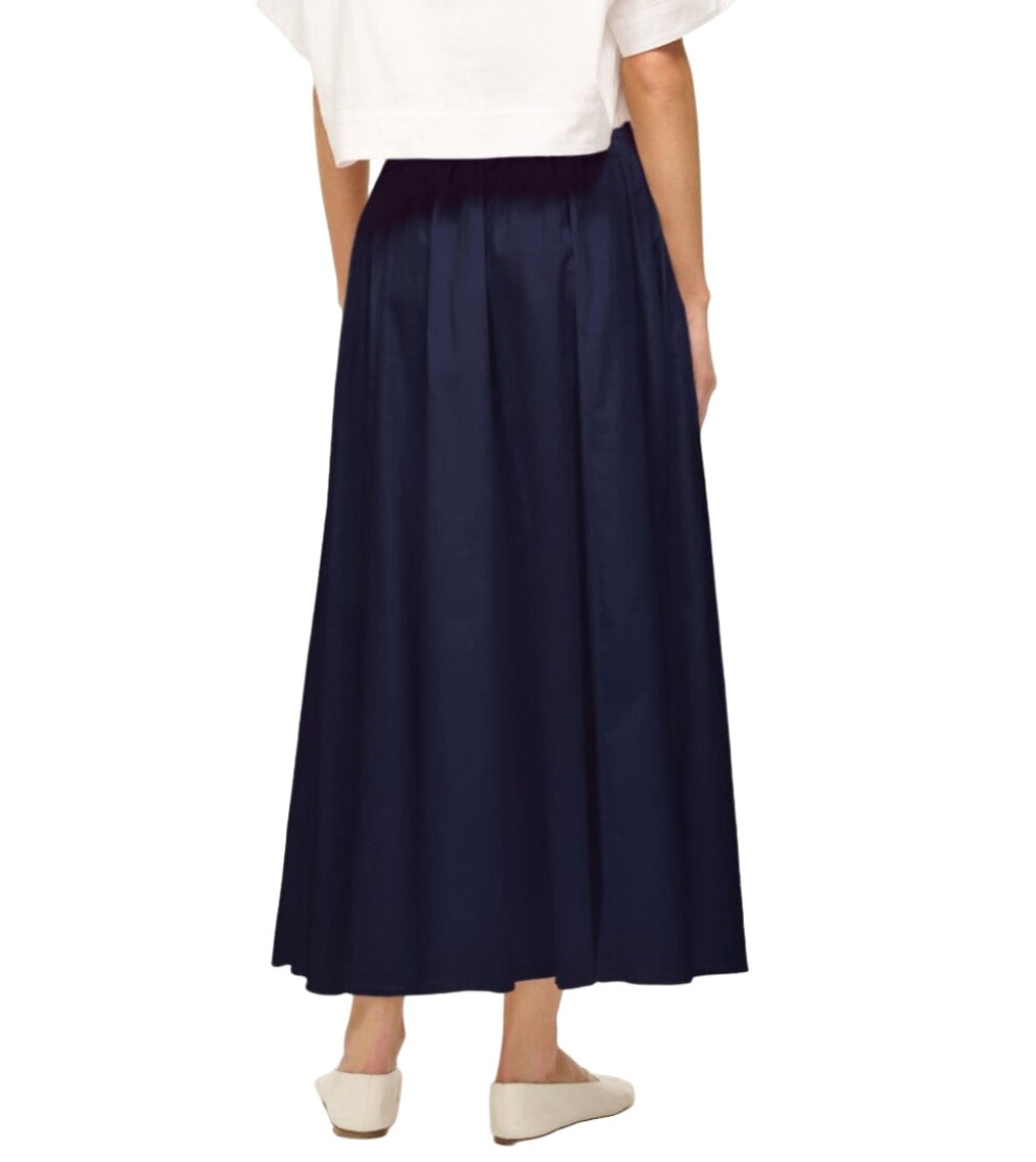 A person is shown from the back, wearing a white top, a long Staud Eden Skirt with an adjustable drawstring waistband, and white shoes. This stylish combination is a summer essential for any wardrobe.