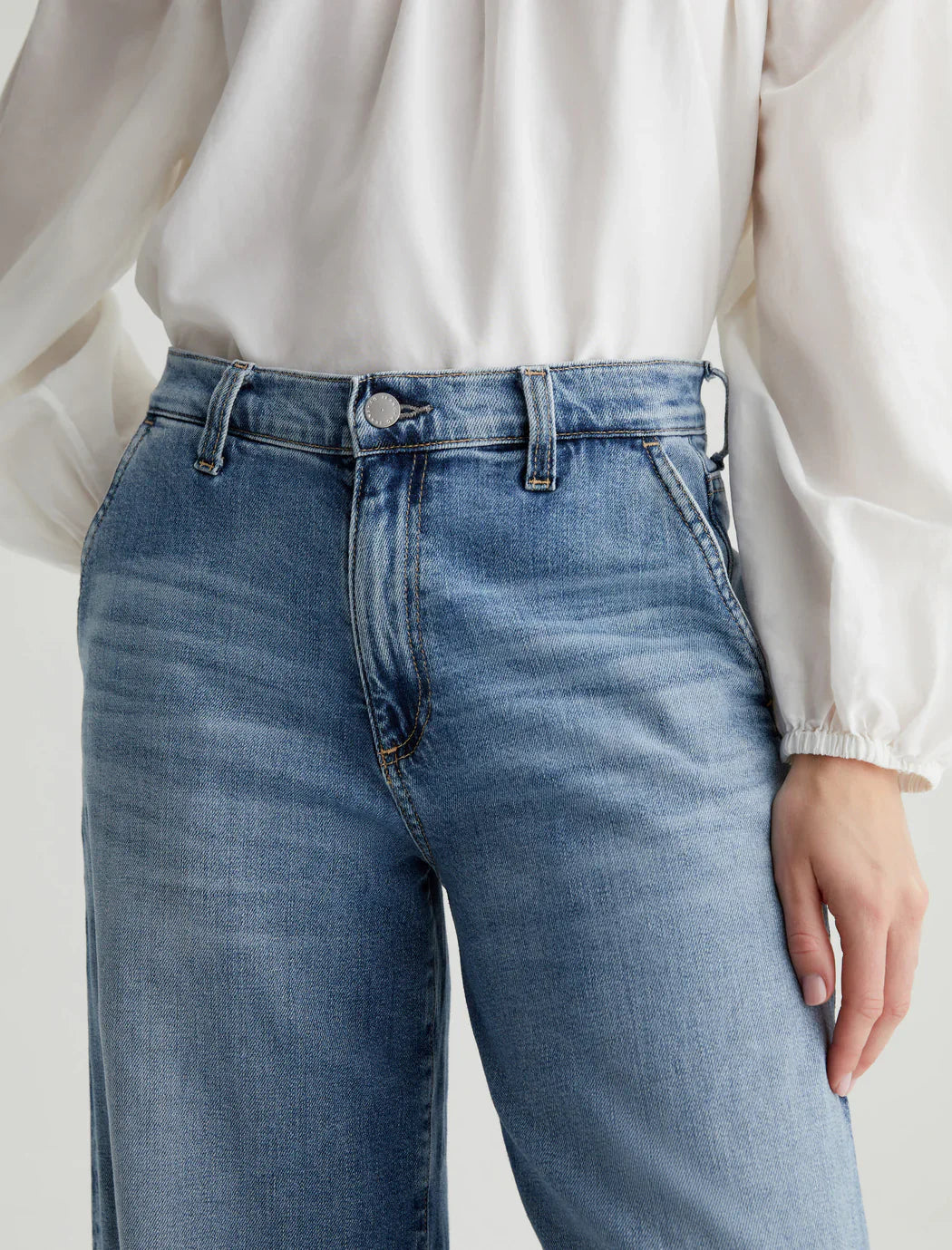 Close-up of a person wearing AG Stella Jeans in light indigo wash and a white blouse with long, puffy sleeves, tucked into the stretch denim jeans from AG Jeans.