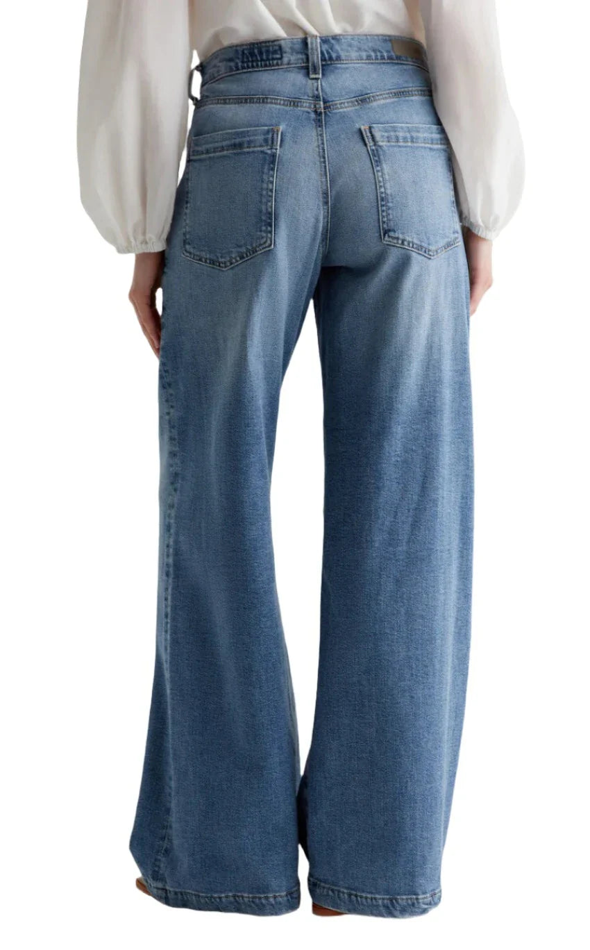 Rear view of a person wearing AG Stella Jeans by AG Jeans in a light indigo wash and a white long-sleeve blouse.