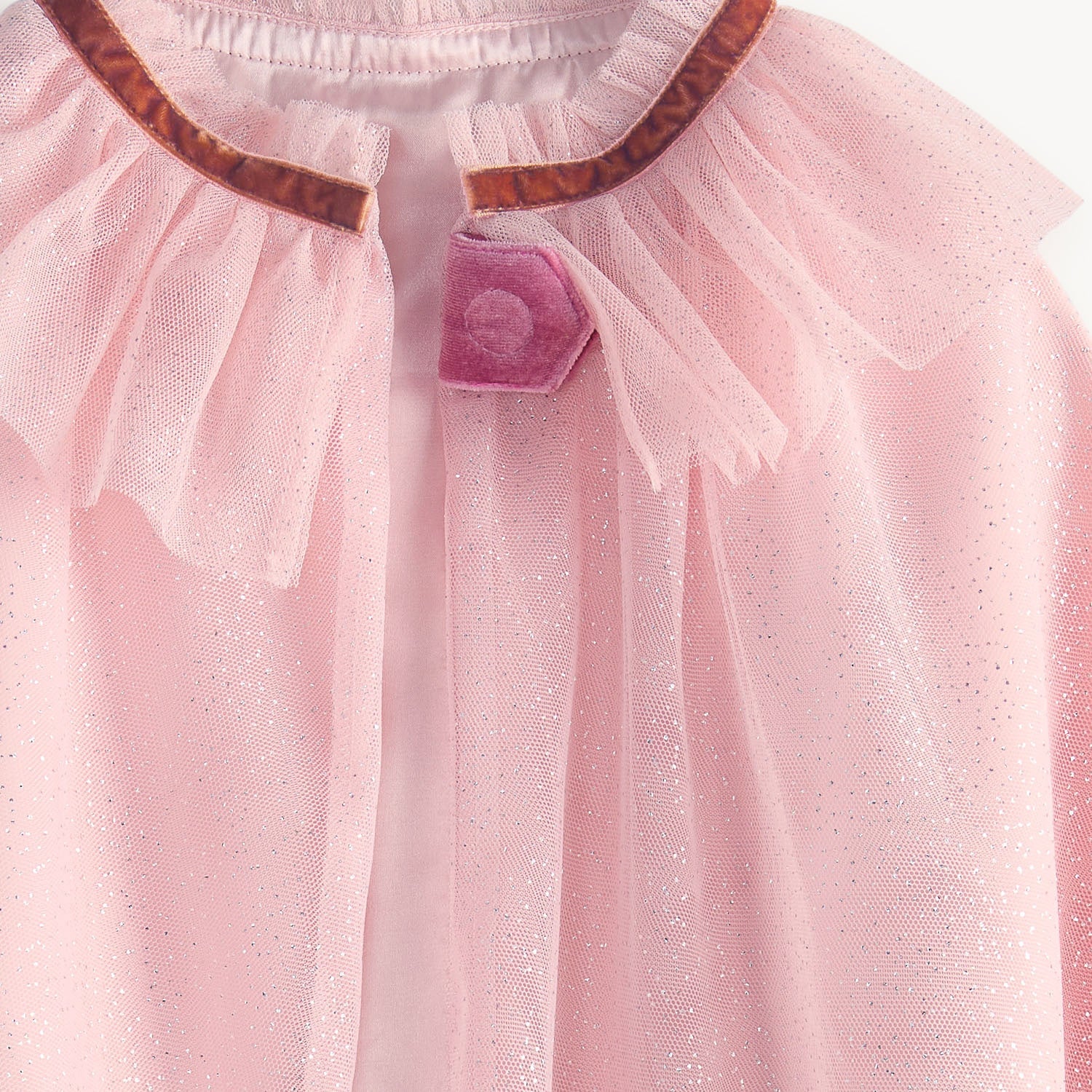 Close-up of the Fairytale Era Tulle Cape by Magnetic Me—a pink costume cape featuring a sheer, ruffled collar, brown trim, and a pink button at the neckline—perfect for pretend play adventures.