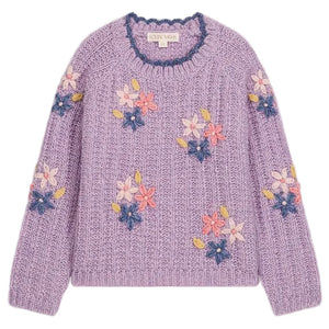 The Girls’ Zuzanna Sweater from Louise Misha is a lilac knit sweater with long sleeves, featuring a crocheted scalloped neckline and detailed with pink, white, and blue handmade floral embroidery, finished with a label at the neckline.