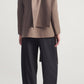 Back view of a person wearing a brown virgin wool Kallmeyer Sablier Scarf Blazer with an integrated scarf draped over the shoulder, paired with black wide-leg trousers.