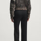A person seen from behind, wearing a black patterned sweater and black straight-leg Heidi Trousers by Kallmeyer with a center crease.