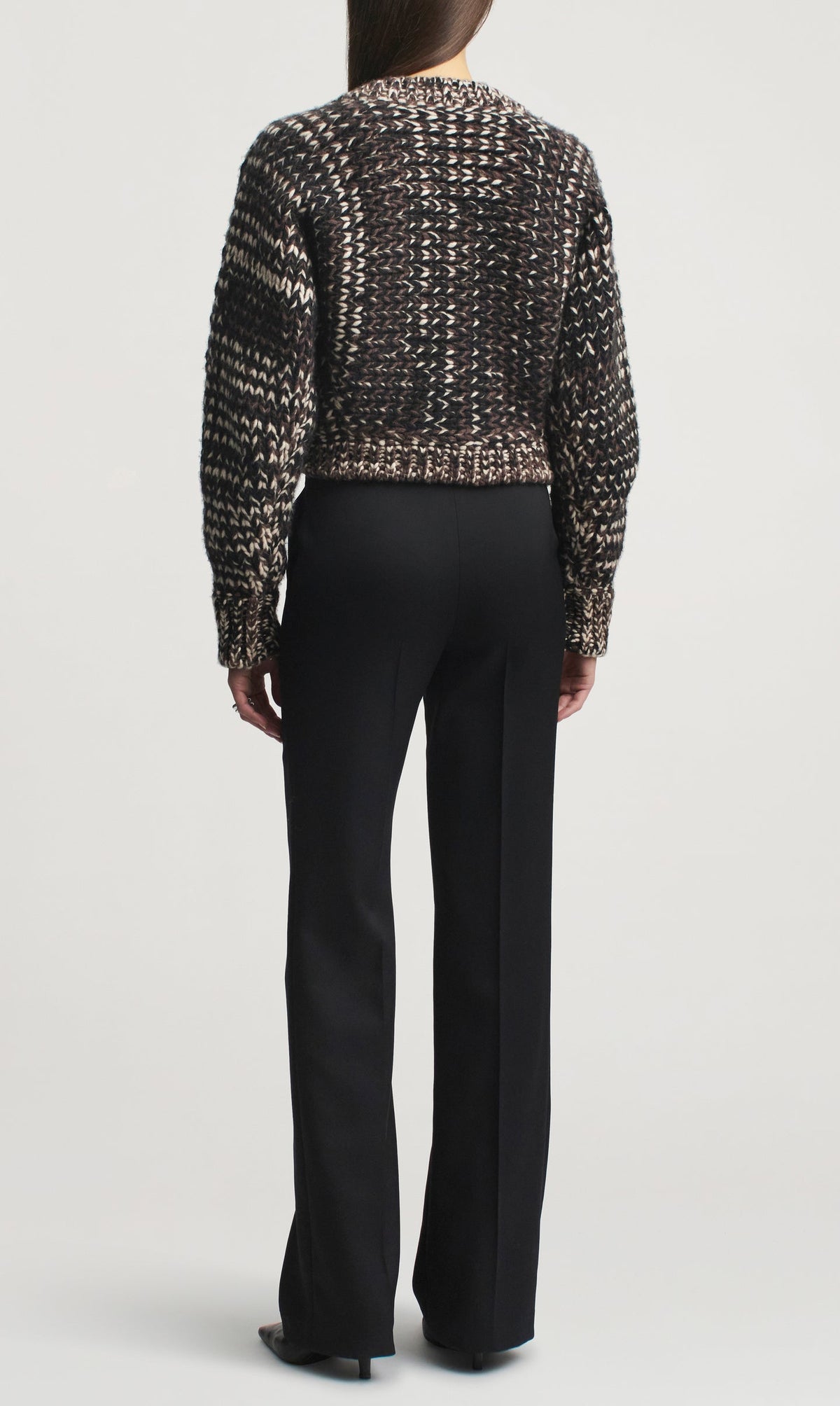 A person seen from behind, wearing a black patterned sweater and black straight-leg Heidi Trousers by Kallmeyer with a center crease.