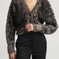 A person wearing a brown and cream cable-knit V-neck cardigan paired with black Kallmeyer Heidi Trouser straight-leg trousers.