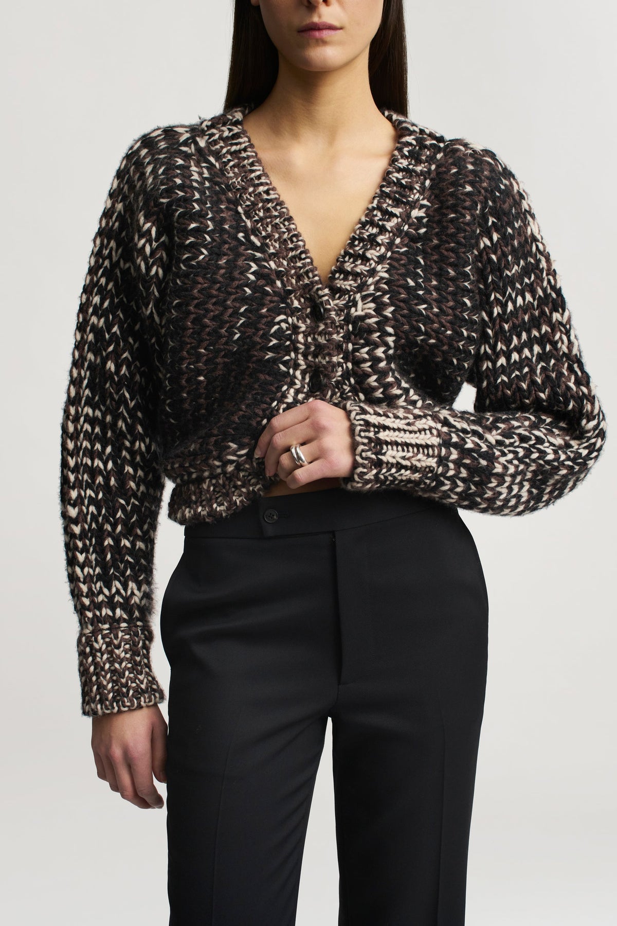 A person wearing a brown and cream cable-knit V-neck cardigan paired with black Kallmeyer Heidi Trouser straight-leg trousers.