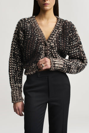 A person wearing a brown and cream cable-knit V-neck cardigan paired with black Kallmeyer Heidi Trouser straight-leg trousers.