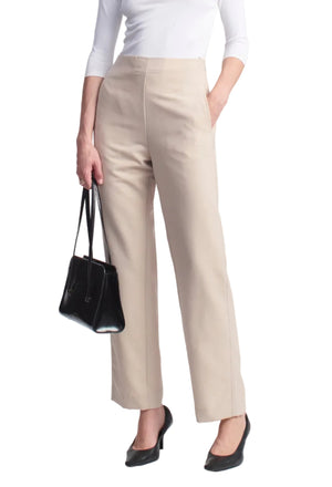 Person wearing light beige, wool gazar Nadja Trouser, high-waisted and cropped at the ankle, with a white long-sleeve top, black pumps, and a black handbag.