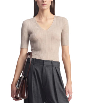 A woman wearing the Kallmeyer Pika Short Sleeve V-Neck, a fitted, ribbed beige pointelle knit top with a subtle deep V neckline, paired with high-waisted charcoal trousers and holding a dark brown handbag.