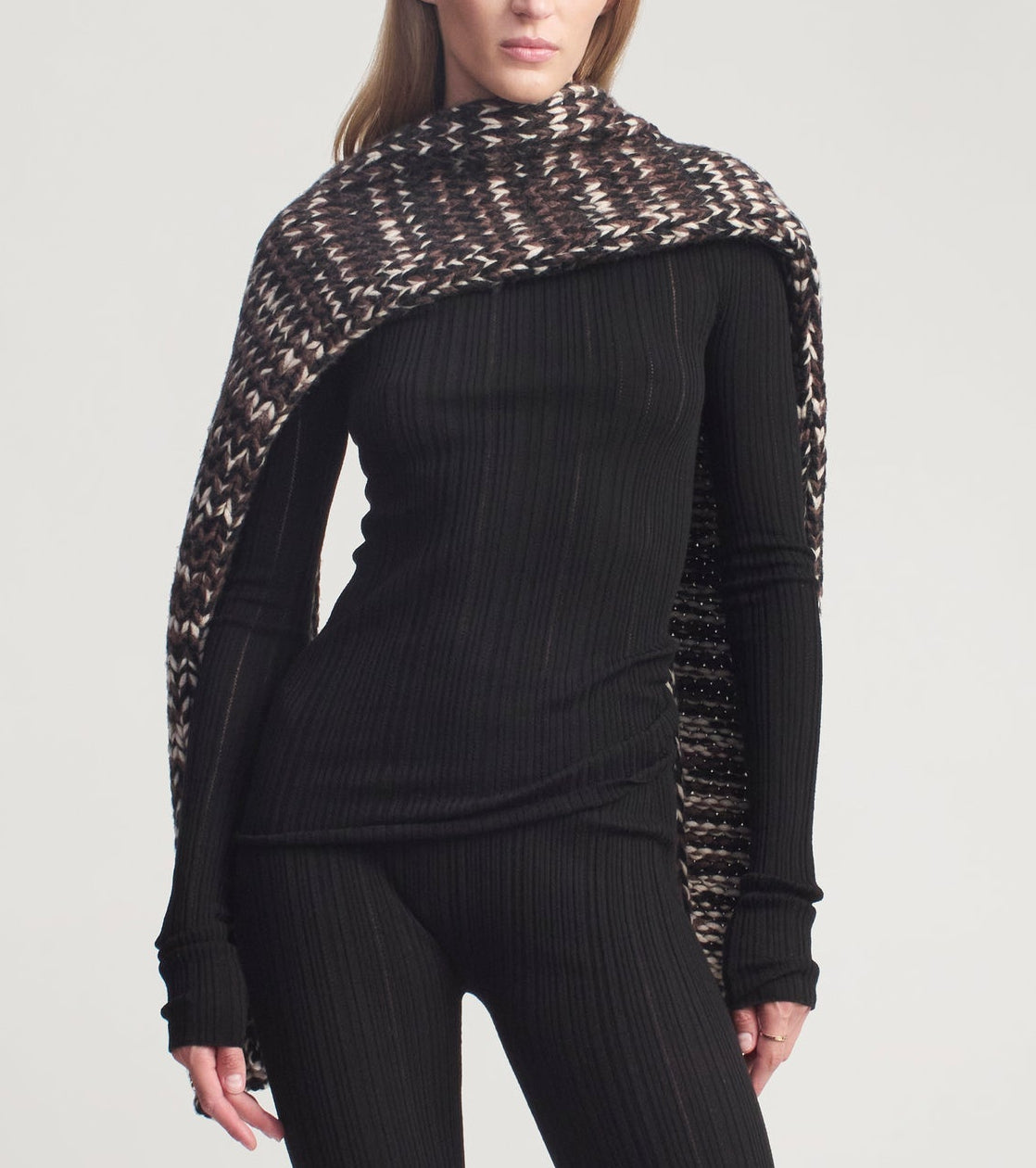 A person wearing a black ribbed long-sleeve top and matching leggings, styled with a brown and white patterned Kallmeyer Kiva Scarf draped over their shoulders.