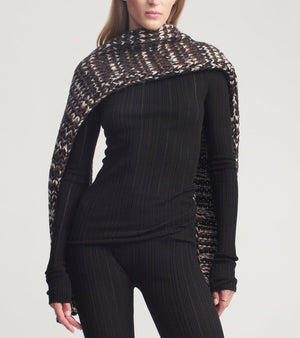 A person wearing a black ribbed long-sleeve top and matching leggings, styled with a brown and white patterned Kallmeyer Kiva Scarf draped over their shoulders.