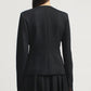 A woman with straight brown hair is shown from behind, wearing the Kallmeyer Tilda Jacket and skirt in classic black Grampians Twill against a plain light background.