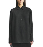 A person wearing the Kallmeyer Mollie Button Down, a relaxed fit black shirt with subtle vertical dotted lines and a collared neckline, stands against a plain white background.