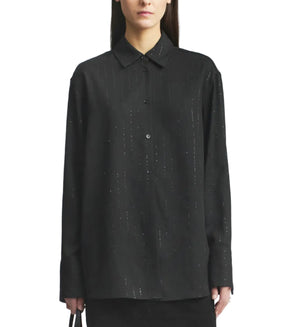 A person wearing the Kallmeyer Mollie Button Down, a relaxed fit black shirt with subtle vertical dotted lines and a collared neckline, stands against a plain white background.