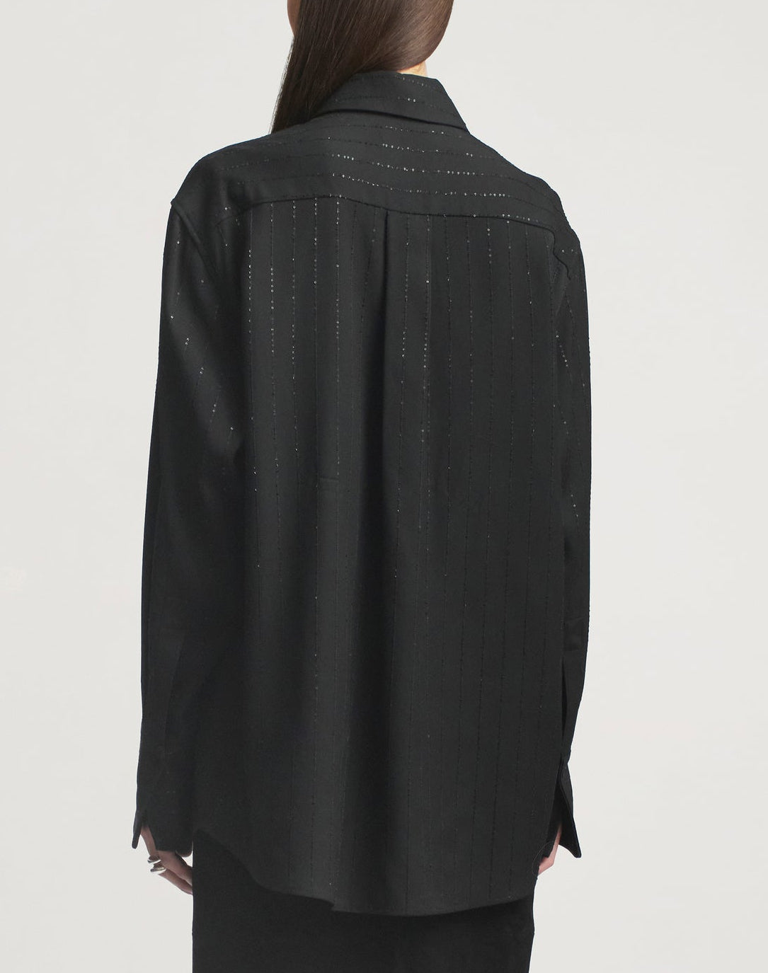 A person is seen from the back against a plain background, wearing the Kallmeyer Mollie Button Down—a relaxed fit black shirt featuring subtle vertical stripes.