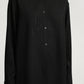 A person wearing the Kallmeyer Mollie Button Down, a relaxed fit black shirt with subtle vertical pinstripes, stands against a plain background.