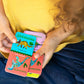 A child, wearing a yellow shirt and blue pants, plays with Eeboo’s Giant Shiny Dinosaur Dominos—colorful cards featuring illustrated dinosaurs and their names, all accented with shiny holographic foil for an extra-special learning experience.