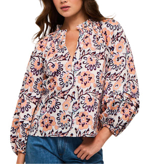 A woman stands confidently with one hand on her hip, wearing the Figue Donna Top—a long-sleeve floral blouse with blouson sleeves and a V-neckline—paired with blue jeans.