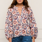 A woman wears the Figue Donna Top, a long-sleeve blouse with a pink, navy, and white floral print, V-neckline, and blouson sleeves for a relaxed fit, paired with blue jeans.